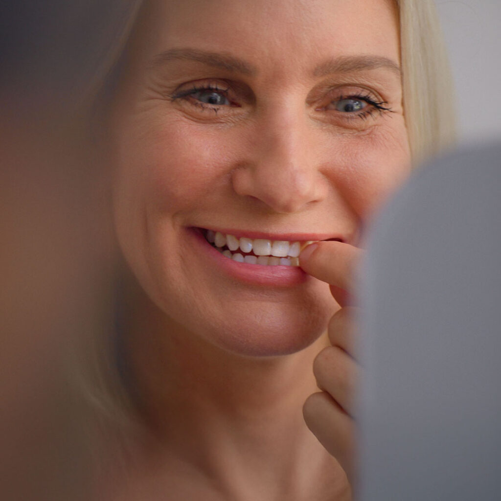 Smiling woman examining her dental implants in a mirror, showcasing confidence and satisfaction with her smile restoration.